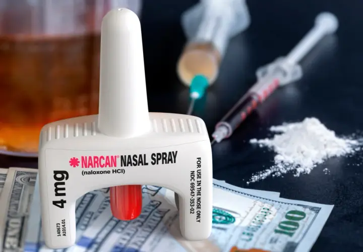 Nasalny spray nalokson, strzykawki i biały proszek na tle banknotów.