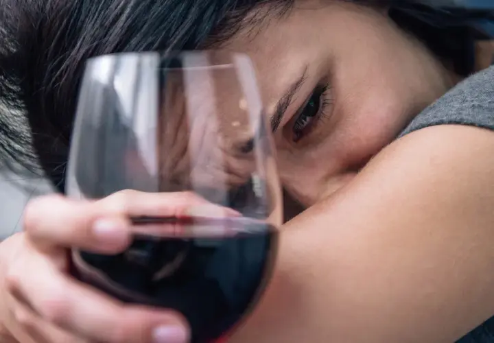 Smutna kobieta z kieliszkiem wina, symbolizująca 6 objawów uzależnienia od alkoholu.