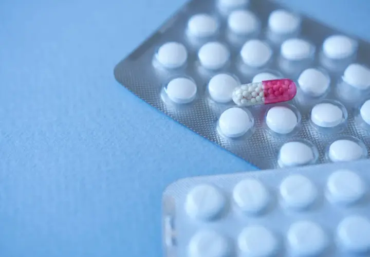 Dwie blistry białych tabletek i jedna kapsułka z różowymi granulkami, przypominająca bromazepam, na niebieskim tle.