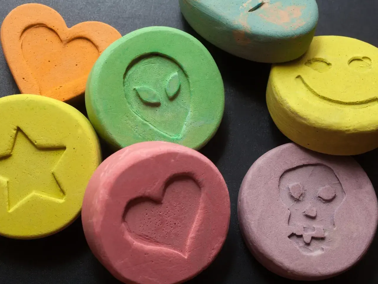 Kolorowe tabletki z symbolami: serce, gwiazda, uśmiech, kosmita, czaszka. Niektóre mogą zawierać mdma.