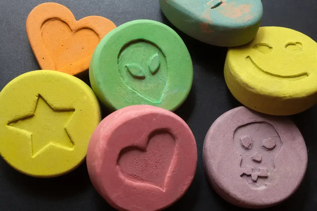 Kolorowe tabletki z symbolami: serce, gwiazda, kosmita, uśmiech, czaszka. To mogą być tabletki MDMA.
