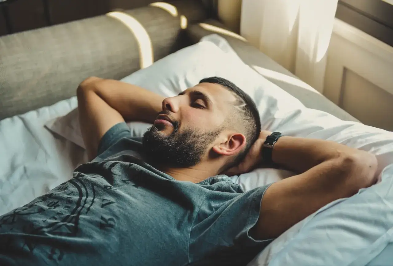 Mężczyzna z zarostem leży na łóżku z rękami za głową. Po długiej nocy pełnej insomnii wreszcie zasnął.